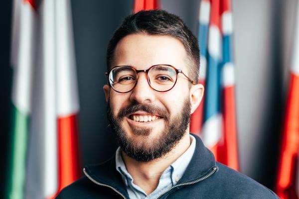 A bearded young man with dark, short hair, wearing glasses, and smiling confidantly.